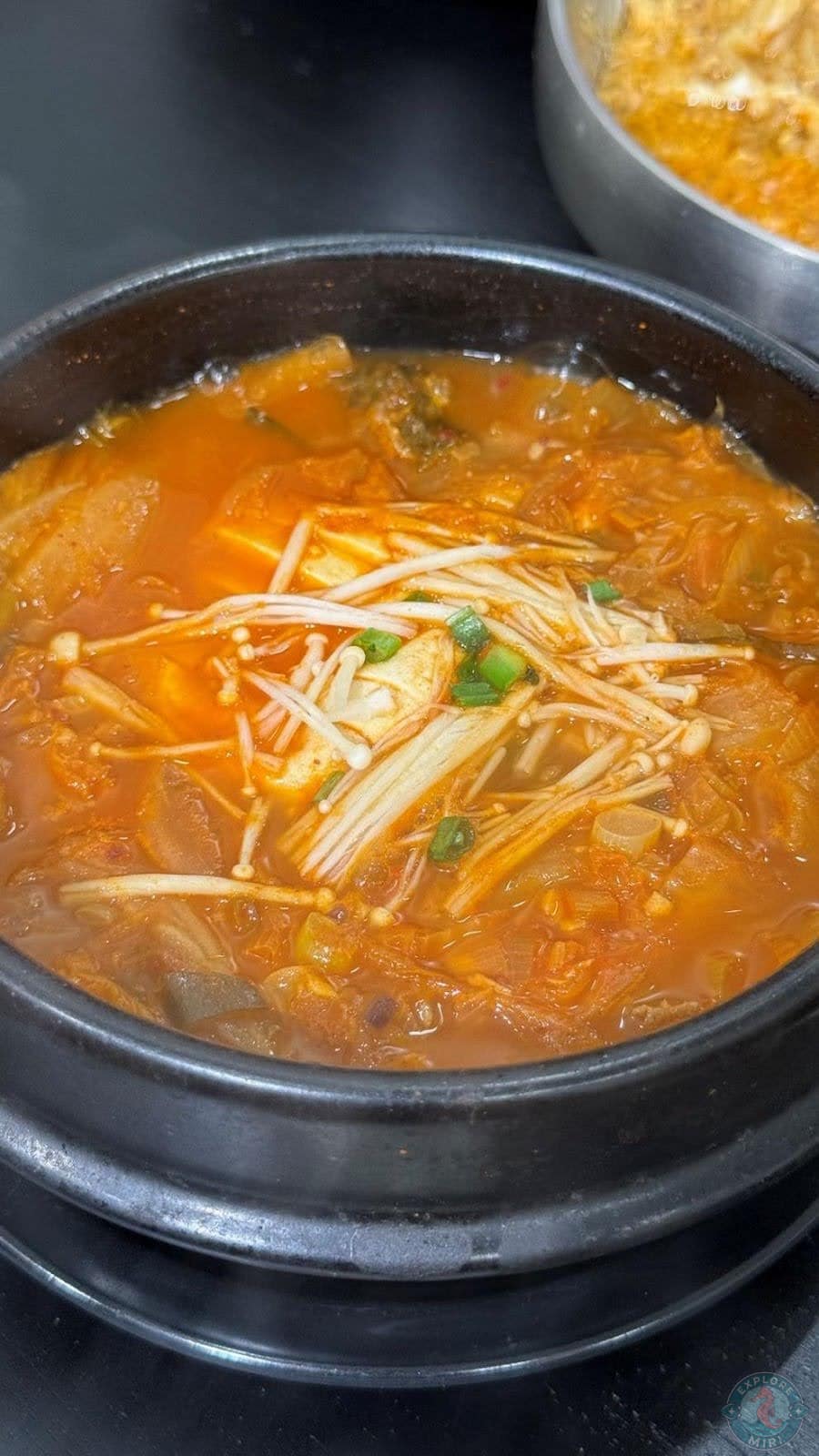 bowl of kimchi soup with vegetables and enoki mushrooms